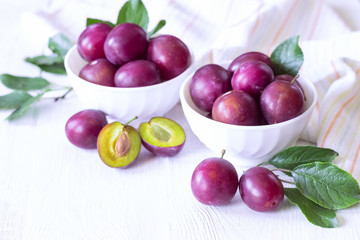ripe purple plums in white cups on a white background. whole plums and half plums in bowls and on the table close-up.
