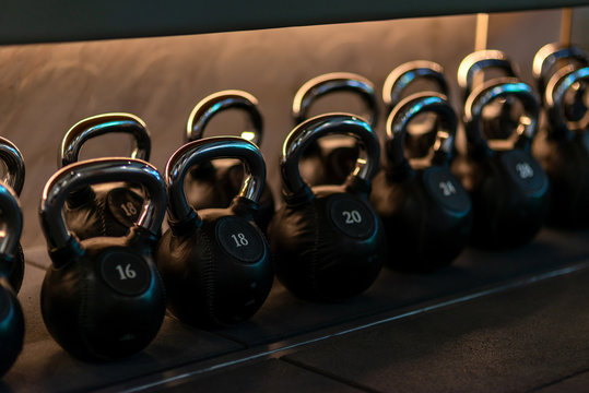 For you to choose. Stylish kettlebells weights made of black leather and iron lying in a row on the shelf in workout gym. Sport, lifting, healthy lifestyle concept. Horizontal shot.