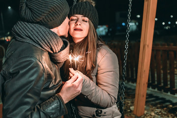 Obraz premium Couple holding sparklers and kissing while swinging in the park. Valentines day