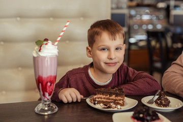 Satisfied boy of 7 years in a restaurant has a cake with a milkshake.