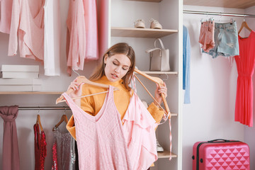 Beautiful young woman choosing clothes from large wardrobe