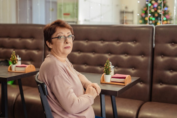 Portrait of a woman of 60 years with short hair wearing glasses in a cafe.