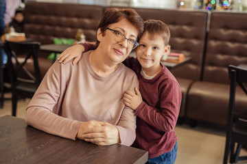 Portrait of a happy grandmother in glasses with a grandson who hugs grandmother. they are looking into the frame