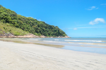 Obraz premium Touristic Brazilian beach on a sunny day of the Paulista coast. View of a beach with no people, calm sea and few waves at Praia do Guaiuba beach - Guaruja SP Brazil.