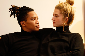 Young intercultural caucasian-hispanic student couple posing happily on a brown leather sofa.