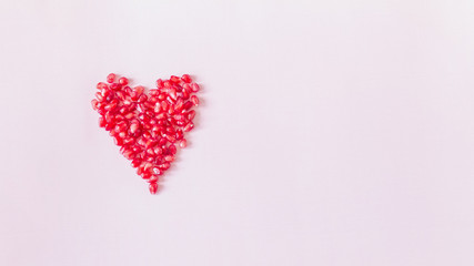 abstract delicate pink background with a heart lined with pomegranate seeds top view. pomegranate seeds lay flat. copy space.
