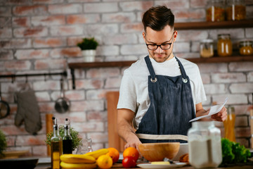 Portrait of handsome man in kitchen. Young man cooking while reading recipe. 