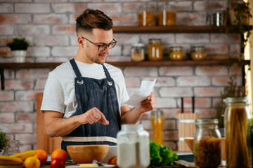 Fototapeta na wymiar Portrait of handsome man in kitchen. Young man cooking while reading recipe. 