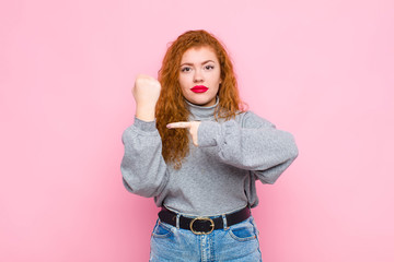 young red head woman looking impatient and angry, pointing at watch, asking for punctuality, wants...