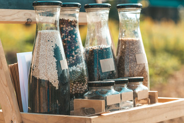 Precise care for producing more. Different kinds of natural grain seed consisted of white, red, black bean and soybean seeds in glass bottles on wooden support outdoors. Agriculture, farming concept