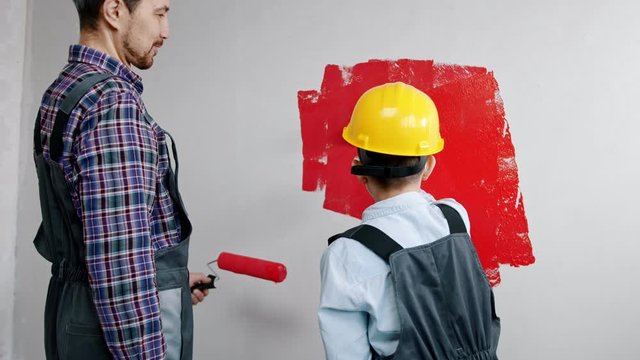 A little boy painting walls with red paint - his father watching him