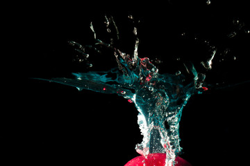 The red object falls into the black water until a sponge splits beautifully on a black background.