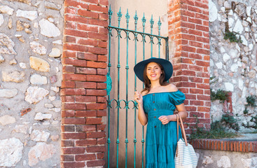 Young and beautiful brunette girl in dress and hat walking outdoor in the street. Nice, France. Summer vacation, traveling and tourism.