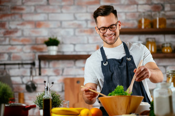 Young man making meal. Chef preparing salad in modern kitchen