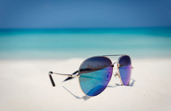 Close up aviator sunglasses in sand on sunny tropical ocean beach