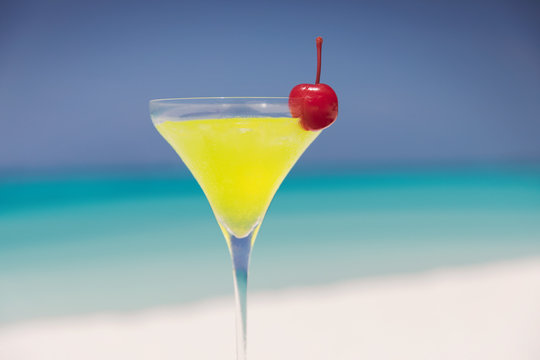 Close up yellow cocktail with cherry in martini glass on sunny tropical beach