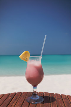 Pink cocktail with pineapple slice and straw on sunny tropical ocean beach