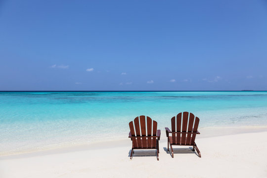 Two adirondack chairs on sunny, tranquil beach overlooking blue ocean, Maldives, Indian Ocean