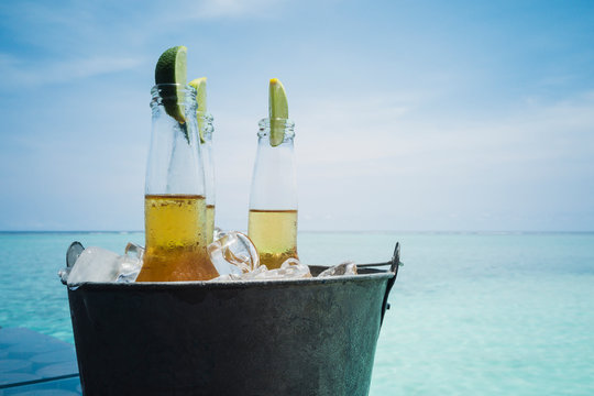 Lime slices in beer bottles on ice on tranquil ocean beach, Maldives, Indian Ocean