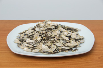 Many empty shells of sunflower seeds on white plate.