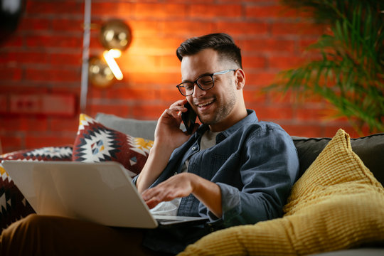 Young Man Working From Home. Businessman At Home On Sofa With Laptop And Phone. 