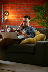 Fototapeta premium Young man working from home. Businessman at home on sofa with laptop and phone. 