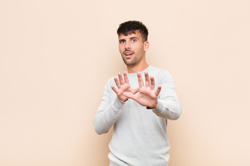 young handsome man feeling terrified, backing off and screaming in horror and panic, reacting to a...