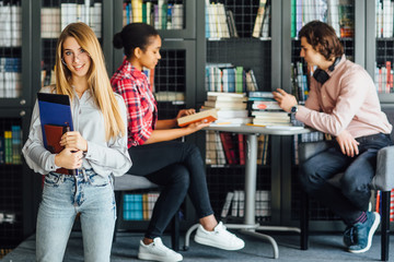 People, knowledge, education and school concept - happy blonde woman posing with book in library.