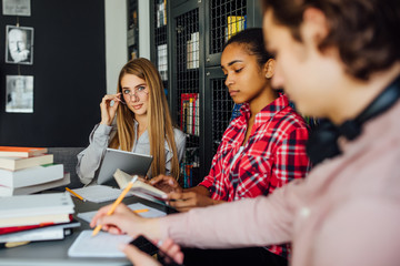 Group of friends having a coffee break in library and using smart phone.