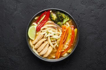 Chicken Thukpa in black bowl at dark slate background. Chicken Thukpa is Tibetan cuisine noodle soup with vegetables and chicken meat. Top view