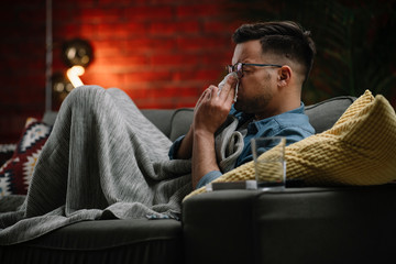 Fototapeta premium Young sick man sitting on sofa.