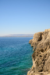view of Syracuse in the distance from the sea with rocks in the foreground