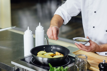 Male chef cooking fresh potato, sauce in restaurant kitchen. Cook at work during dinner service....