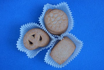 brown dry cookies with sugar in three white paper packages on a stand on a blue table