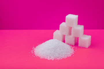 Cubes of white sugar and granulated sugar on an pink background