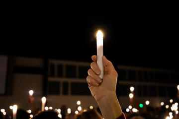 One single hand arm holding up a LED candle amongst a crowd of lights at a candlight service vigil - obrazy, fototapety, plakaty