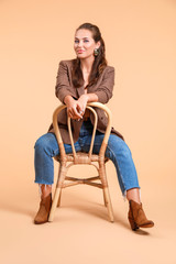 Portrait of fashionable young woman sitting on chair against color background