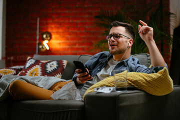 Young man listening music. Attractive man sitting on sofa and listening music in living room.