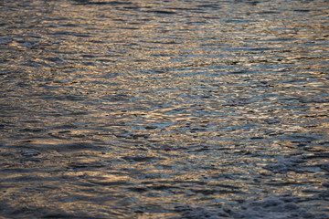 Abstract evening sunset view of small details of river waves with bubbles.