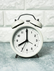 Close-up white alarm clock with brick wall.