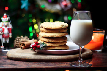 Cookies biscuits for Santa Claus near a christmas tree decorated with Nutcracker, flashing lights,mistletoe and a glass of milk on a wooden tray, atmospheric Christmas picture 