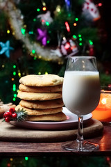 Cookies biscuits for Santa Claus near a christmas tree decorated with flashing lights,mistletoe and a glass of milk on a wooden tray, atmospheric Christmas picture