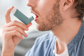 Sick man with asthma inhaler at home, closeup