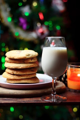 Cookies biscuits for Santa Claus near a christmas tree decorated with flashing lights,mistletoe and a glass of milk on a wooden tray, atmospheric Christmas picture