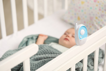 Modern baby monitor on bed with sleeping child