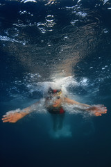 Professional swimmer moving fast in ocean water deep blue color on background, underwater shot