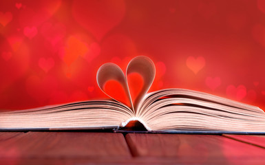 Open book on wooden table on red background