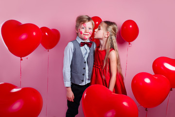 Fototapeta na wymiar Funny little boy with red kisses on the skin and girl in red balloons in the shape of a heart