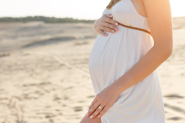 Fototapeta na wymiar hands of a pregnant girl on the tummy, desert