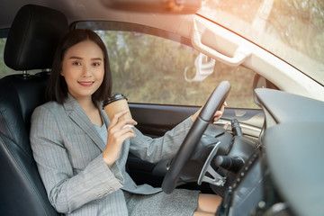Fototapeta na wymiar Asian female driver smiling and drinking coffee in the car, Beautiful girl holding an eco paper coffee cup,looking to camera while driving her car, happy life transport in city